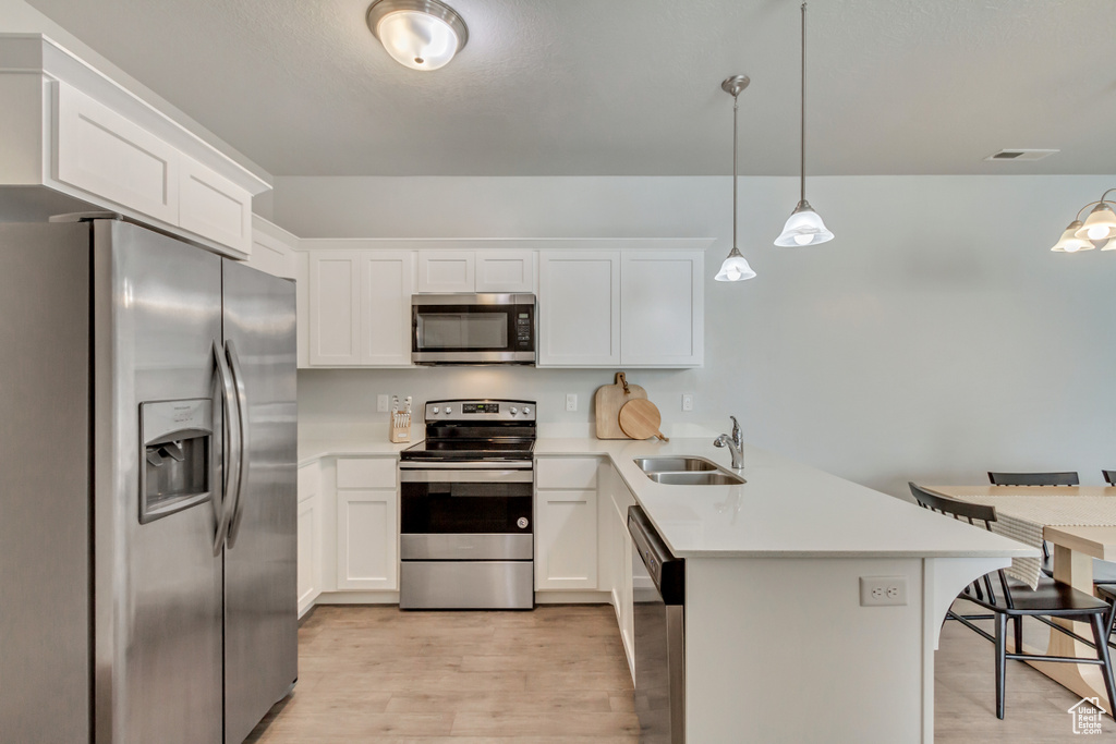 Kitchen featuring stainless steel appliances, sink, a kitchen breakfast bar, decorative light fixtures, and white cabinets