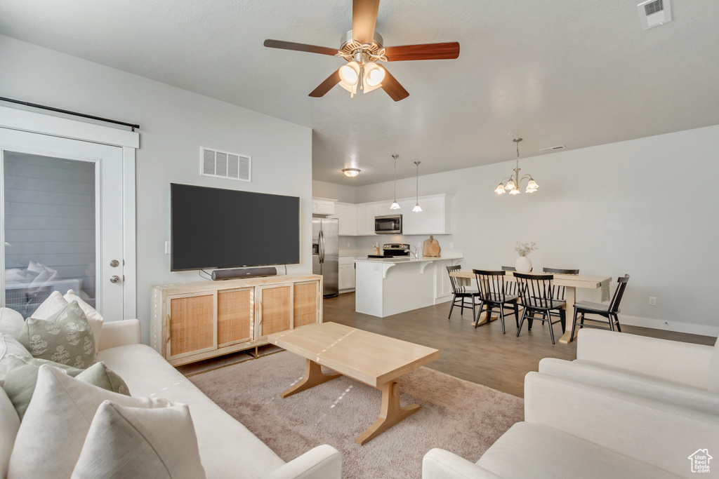 Living room featuring a barn door, hardwood / wood-style flooring, and ceiling fan with notable chandelier