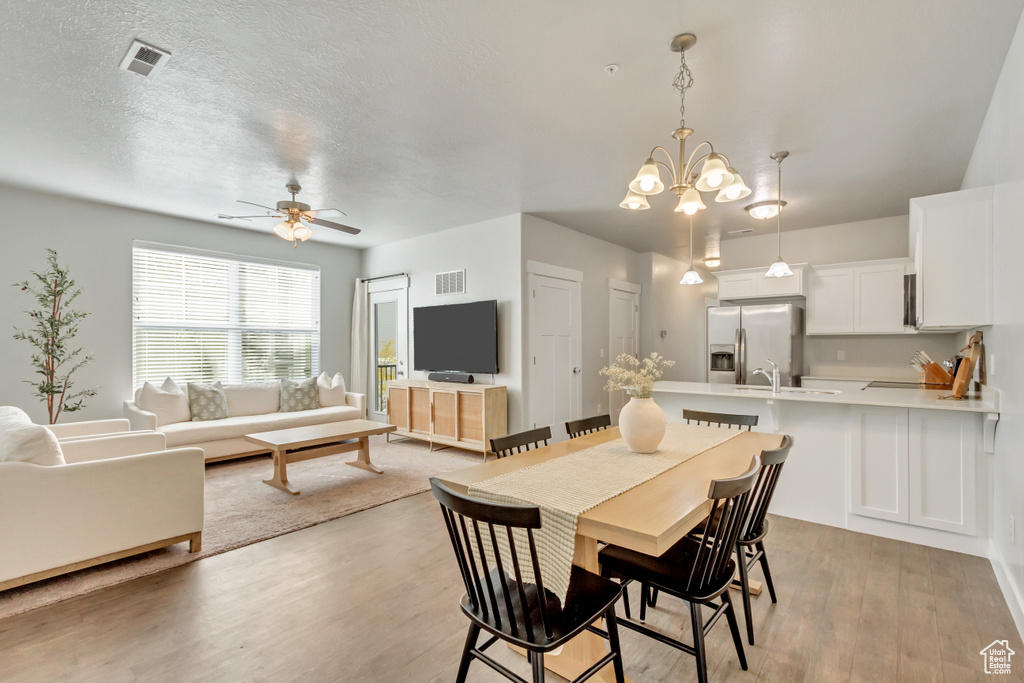 Dining space featuring light hardwood / wood-style floors, ceiling fan with notable chandelier, and a textured ceiling