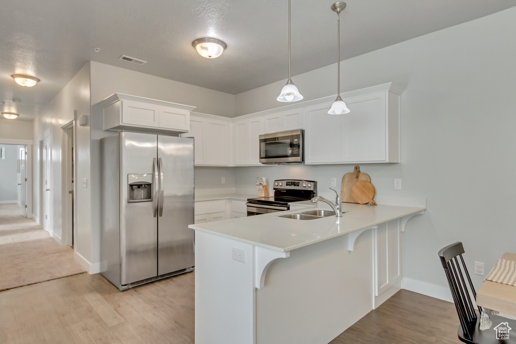 Kitchen with kitchen peninsula, sink, white cabinetry, appliances with stainless steel finishes, and decorative light fixtures