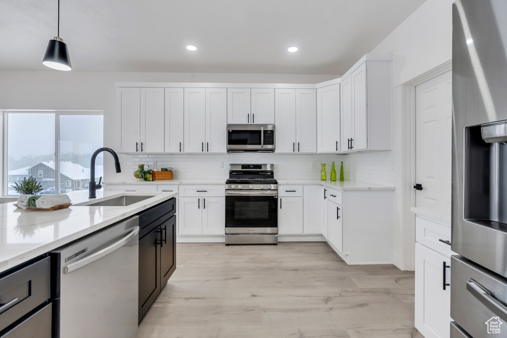 Kitchen featuring stainless steel appliances, decorative light fixtures, sink, light hardwood / wood-style floors, and white cabinets