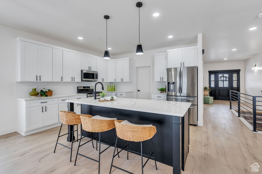 Kitchen with stainless steel appliances, light hardwood / wood-style floors, white cabinetry, and an island with sink