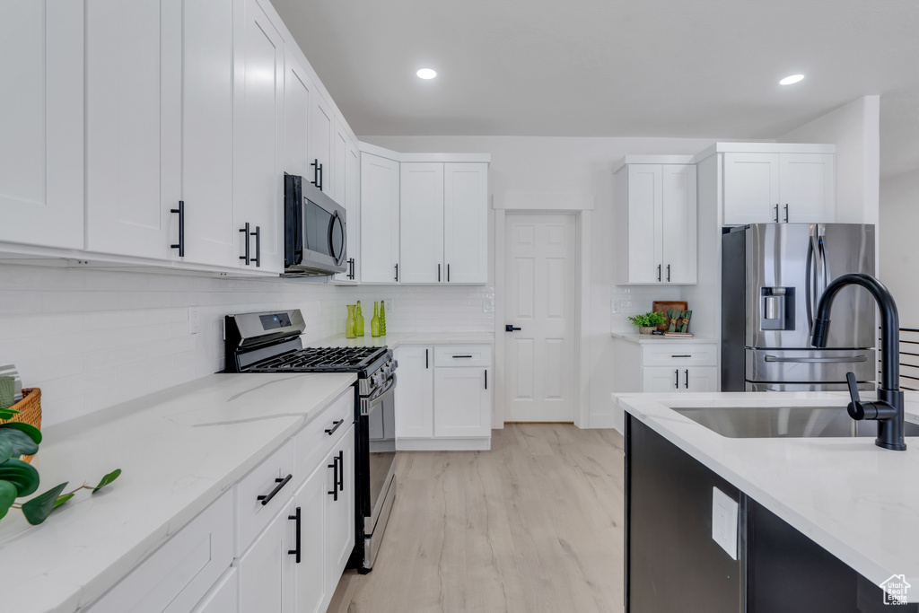 Kitchen featuring white cabinetry, appliances with stainless steel finishes, backsplash, sink, and light hardwood / wood-style flooring