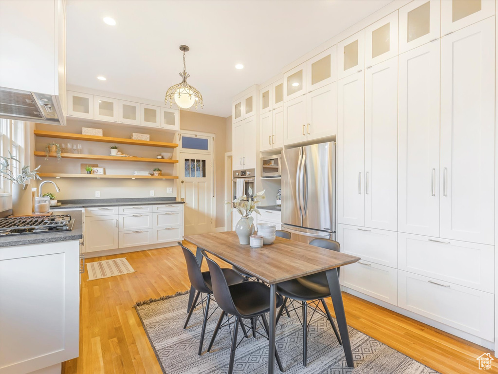 Kitchen with appliances with stainless steel finishes, wall chimney exhaust hood, light hardwood / wood-style flooring, white cabinets, and pendant lighting