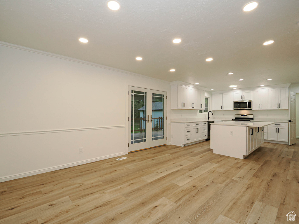 Kitchen featuring crown molding, a kitchen island, appliances with stainless steel finishes, light hardwood / wood-style floors, and white cabinets