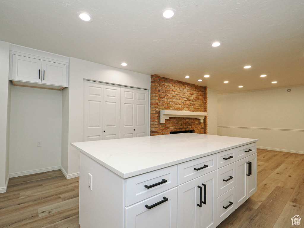 Kitchen with white cabinets, light wood-type flooring, a fireplace, and a kitchen island