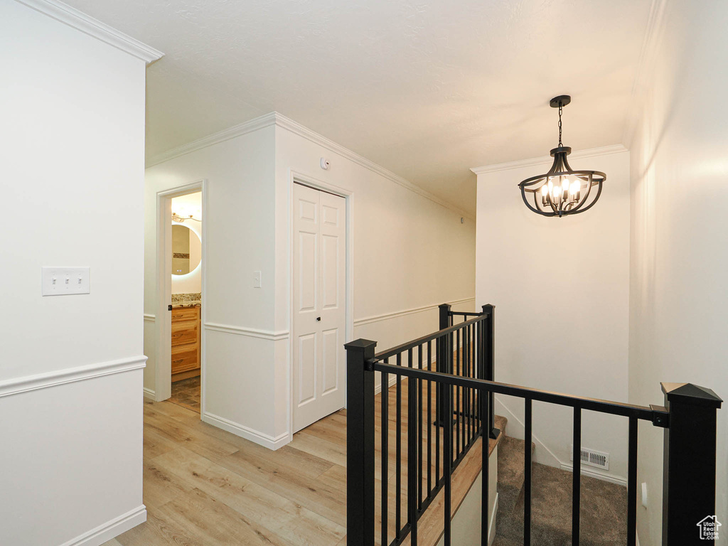 Hallway featuring ornamental molding, light hardwood / wood-style flooring, and a notable chandelier