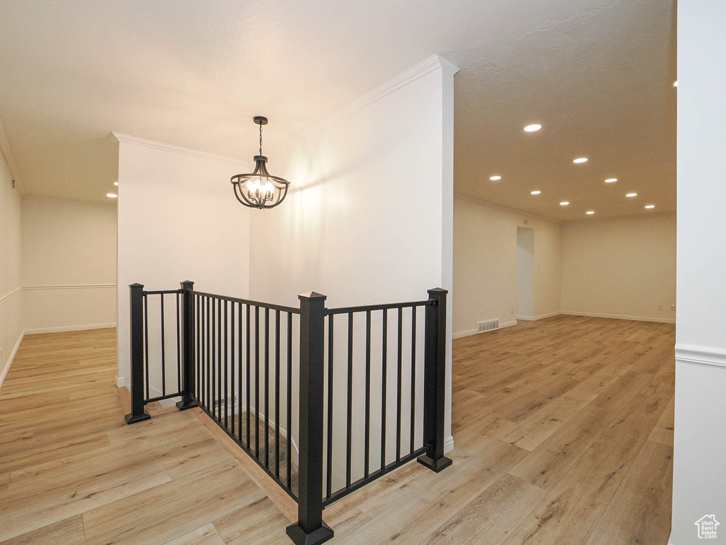 Corridor with light hardwood / wood-style flooring, crown molding, and a notable chandelier