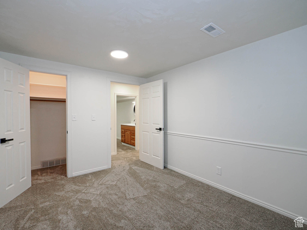 Unfurnished bedroom with light carpet, a walk in closet, and a closet