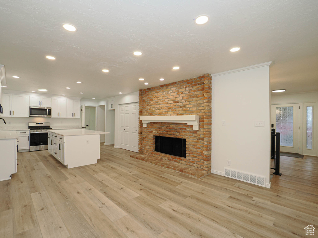 Kitchen with a brick fireplace, light hardwood / wood-style floors, a center island, white cabinets, and appliances with stainless steel finishes