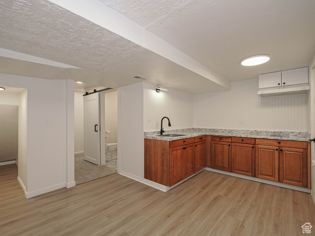 Kitchen featuring light stone counters, light wood-type flooring, a barn door, a textured ceiling, and sink