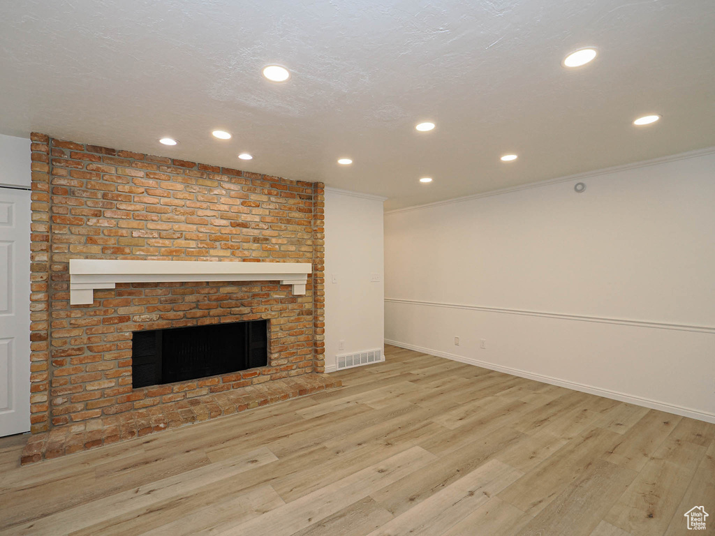 Unfurnished living room featuring a fireplace, light wood-type flooring, and ornamental molding