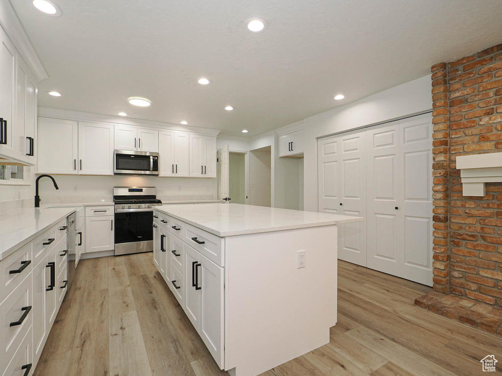 Kitchen with stainless steel appliances, light hardwood / wood-style floors, and white cabinets