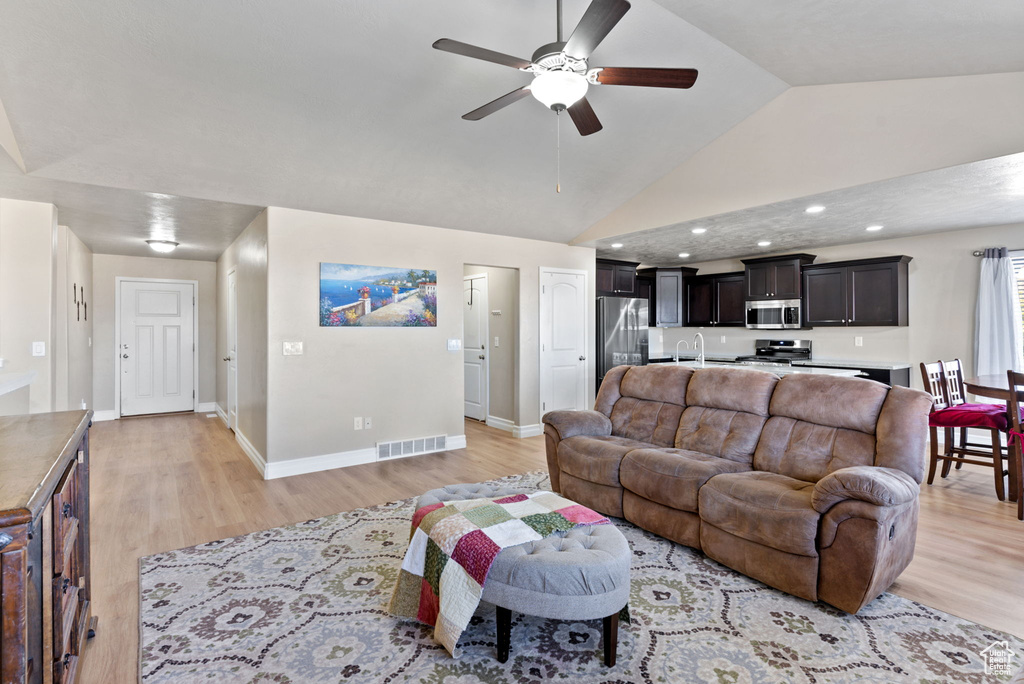 Living room featuring ceiling fan, sink, light wood-type flooring, and vaulted ceiling