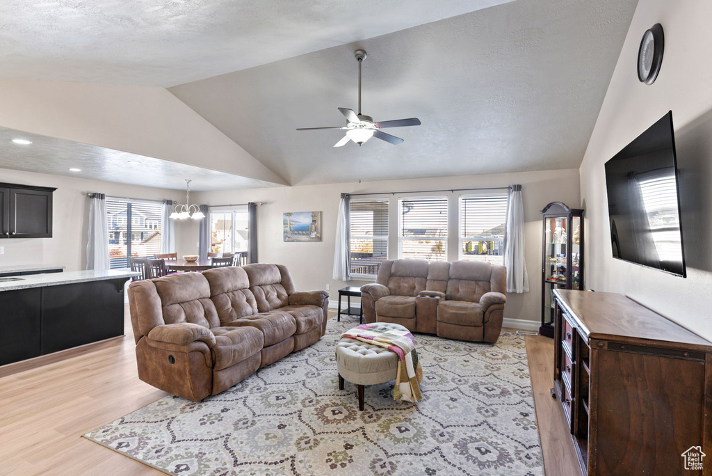 Living room with ceiling fan with notable chandelier, light hardwood / wood-style floors, lofted ceiling, and a textured ceiling