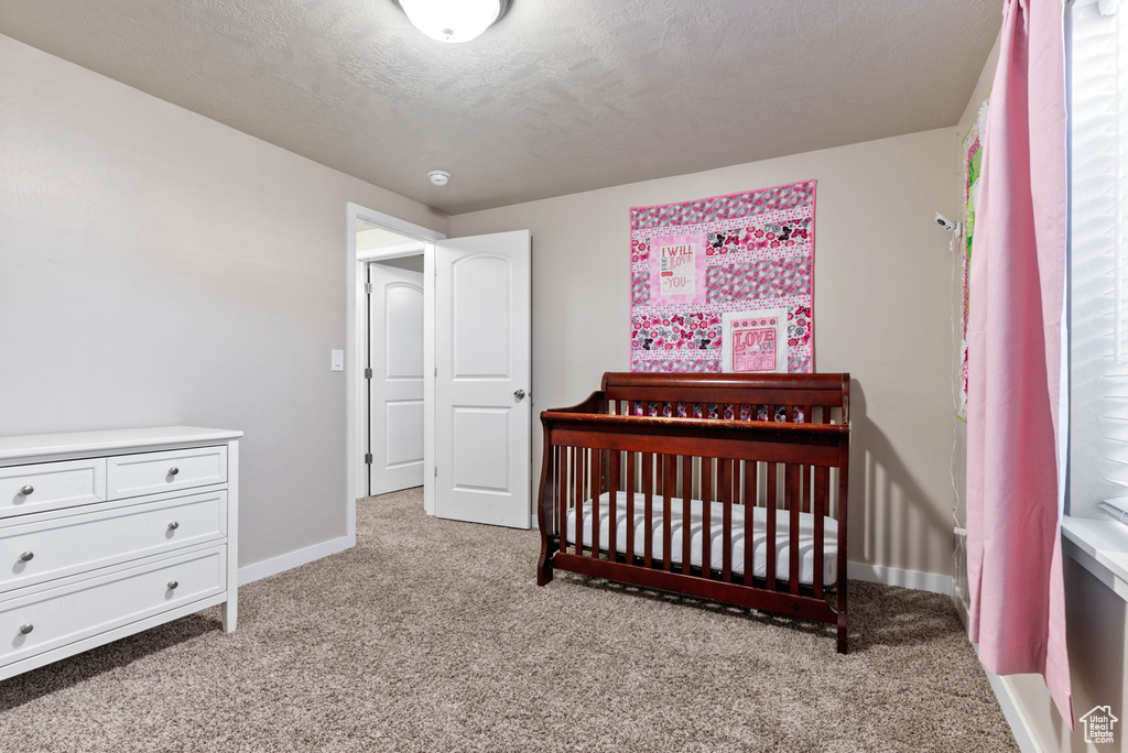 Carpeted bedroom featuring a nursery area and a textured ceiling