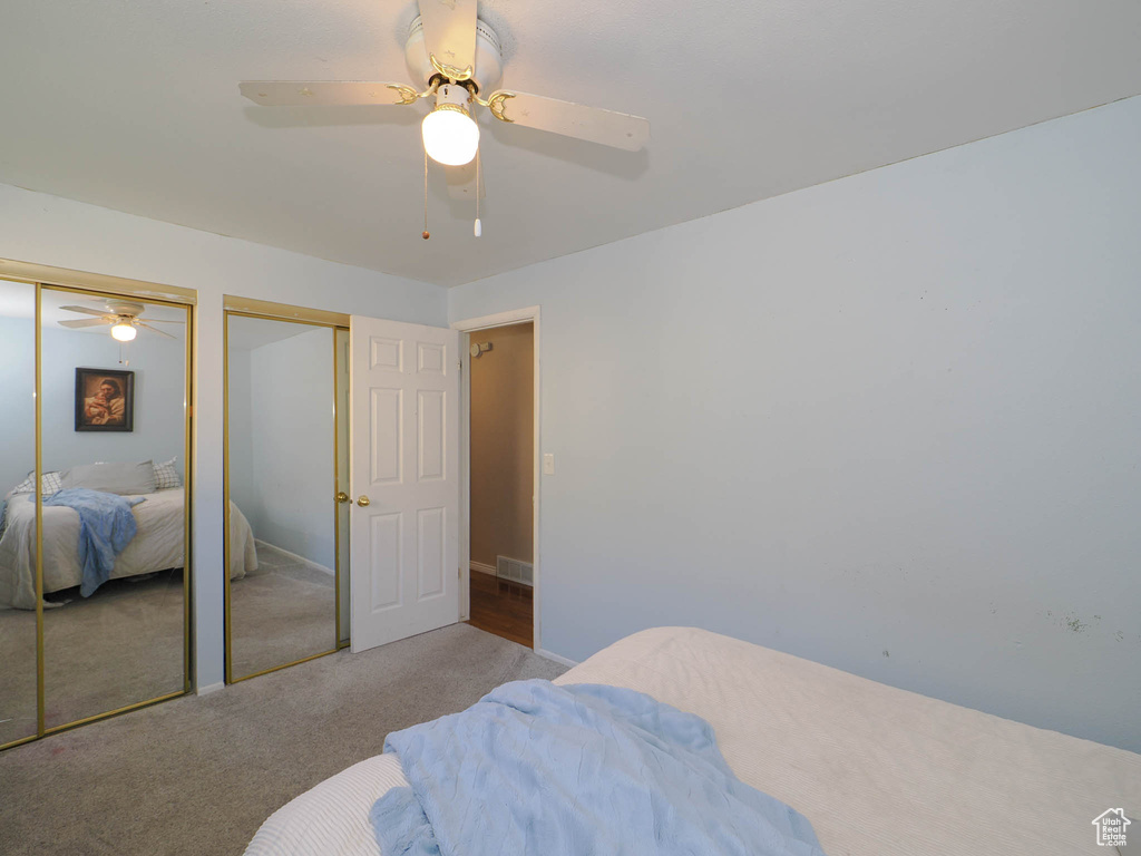 Bedroom with ceiling fan, light carpet, and multiple closets