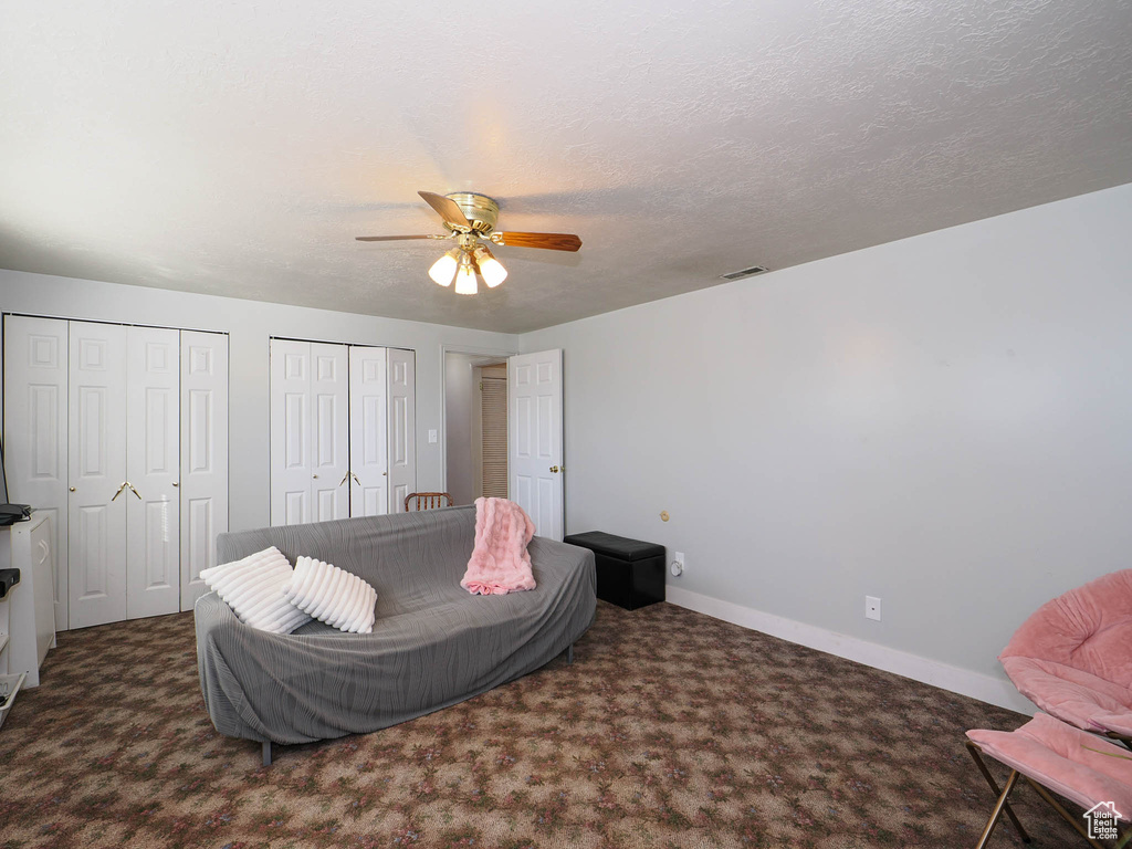 Living area featuring ceiling fan, a textured ceiling, and dark carpet