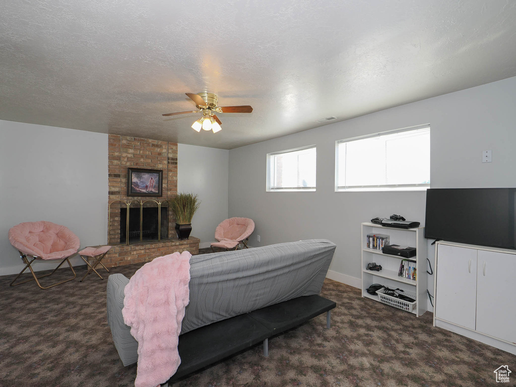 Bedroom featuring a textured ceiling, a fireplace, dark colored carpet, and ceiling fan