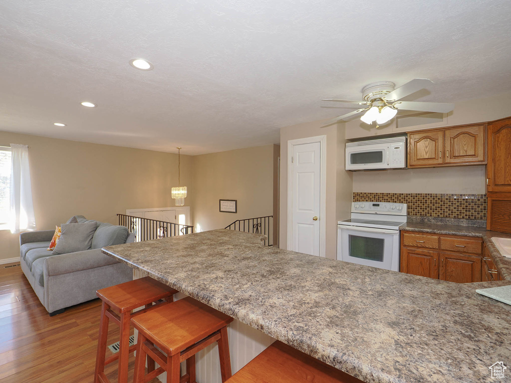 Kitchen with light hardwood / wood-style floors, ceiling fan, a kitchen bar, decorative light fixtures, and white appliances