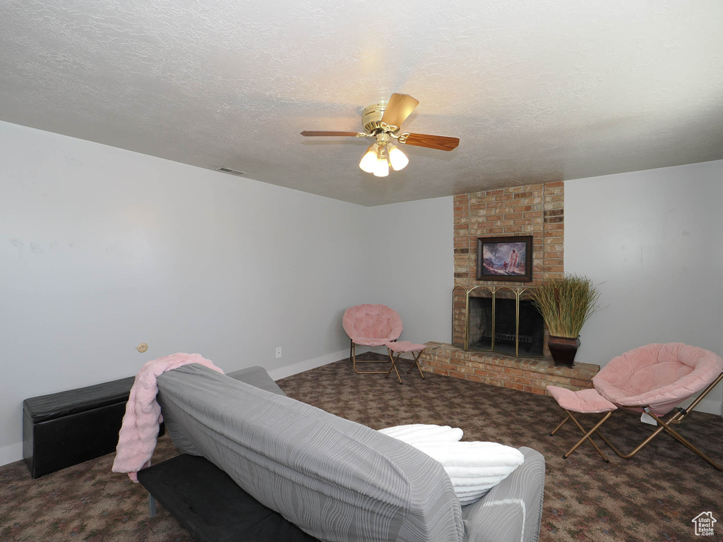 Carpeted living room featuring a textured ceiling, ceiling fan, and a brick fireplace