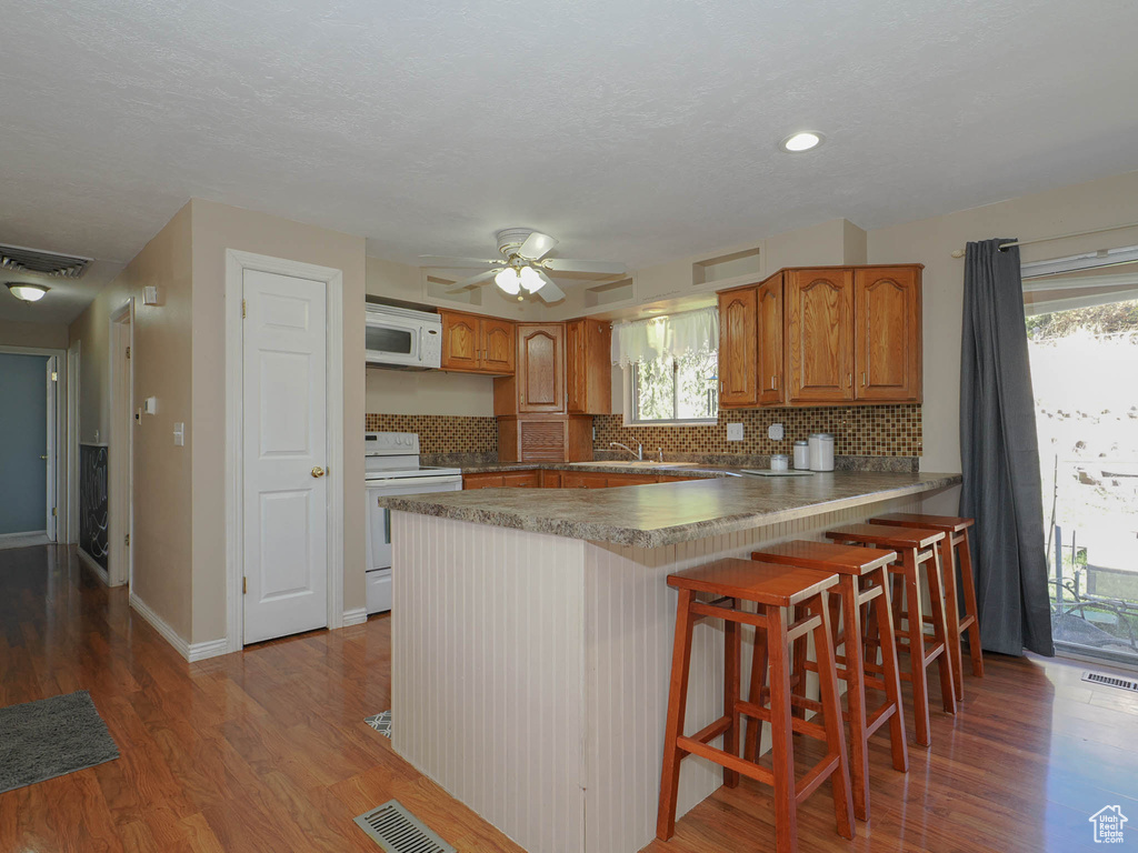 Kitchen featuring a breakfast bar, kitchen peninsula, ceiling fan, wood-type flooring, and electric range