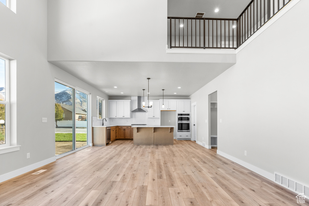 Interior space featuring white cabinetry, a center island, wall chimney exhaust hood, double oven, and light hardwood / wood-style floors