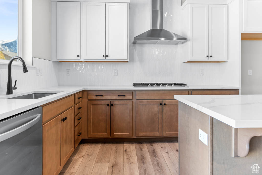 Kitchen featuring sink, stainless steel appliances, wall chimney range hood, light hardwood / wood-style floors, and white cabinets