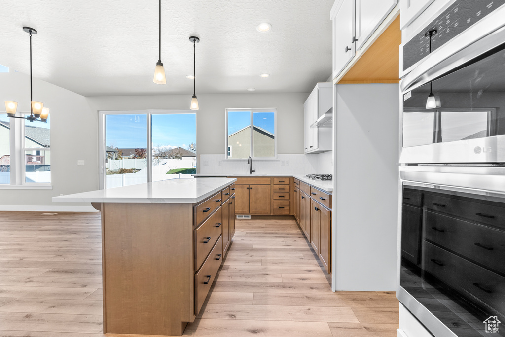 Kitchen featuring white cabinets, a center island, decorative light fixtures, and light hardwood / wood-style flooring