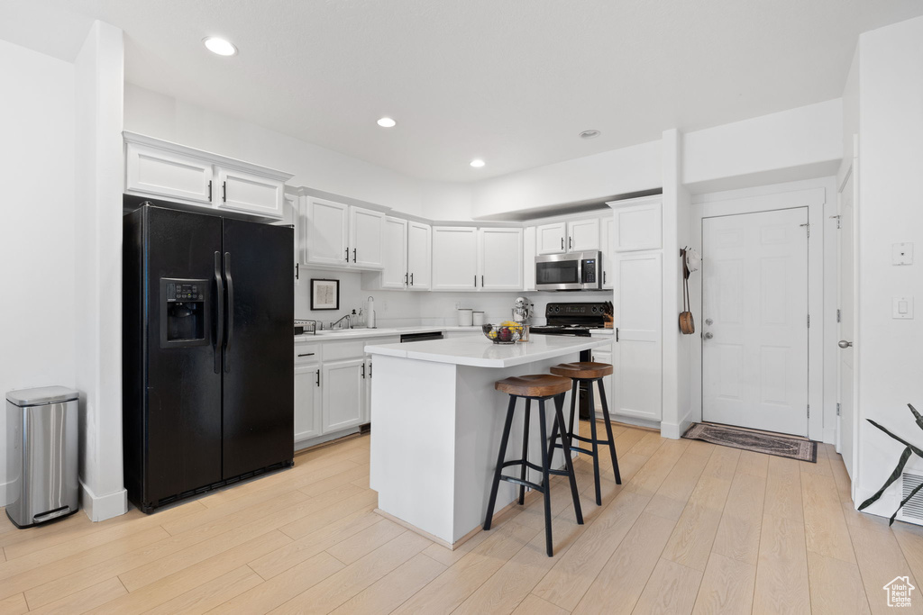 Kitchen with light hardwood / wood-style floors, a center island, black appliances, a breakfast bar area, and white cabinetry