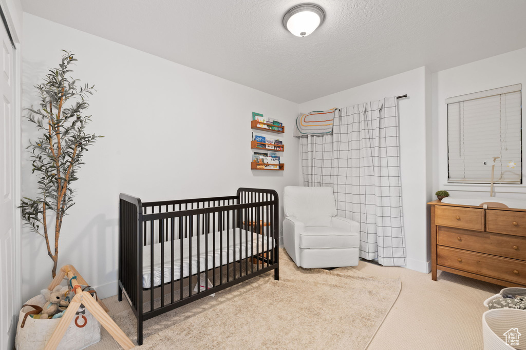 Bedroom featuring carpet, a nursery area, and a textured ceiling