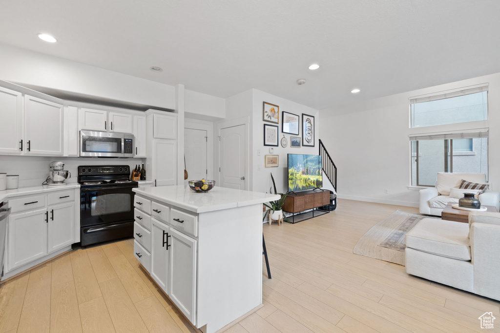 Kitchen featuring black electric range, a center island, white cabinets, a breakfast bar area, and light wood-type flooring