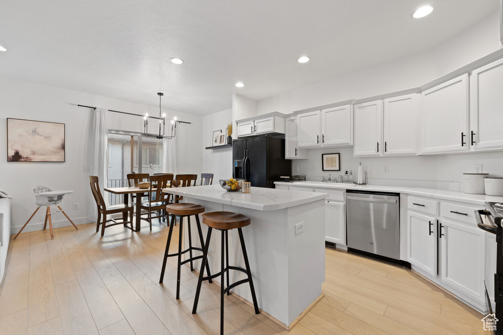 Kitchen with white cabinetry, stainless steel dishwasher, a kitchen island, pendant lighting, and black fridge with ice dispenser