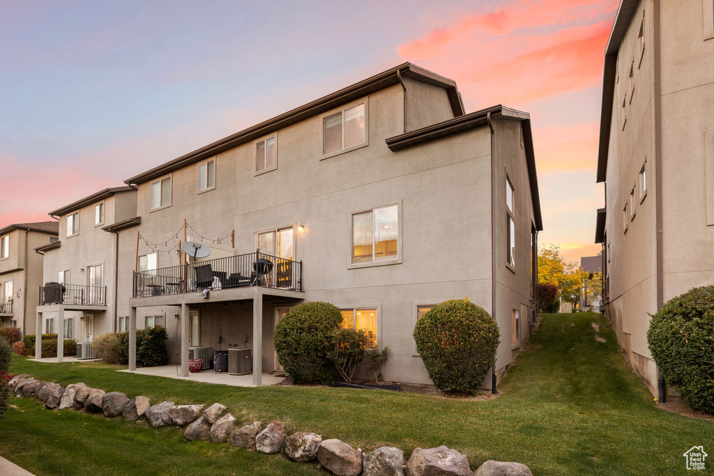 Back house at dusk featuring a patio, a lawn, and cooling unit