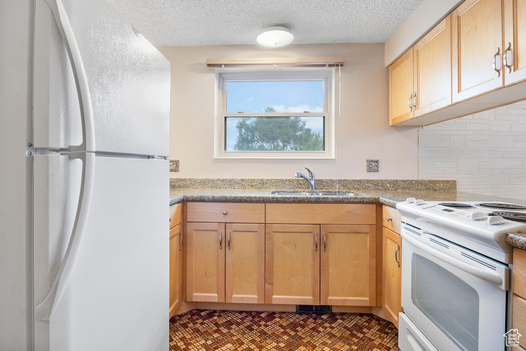 Kitchen featuring backsplash, a textured ceiling, light brown cabinetry, sink, and white appliances