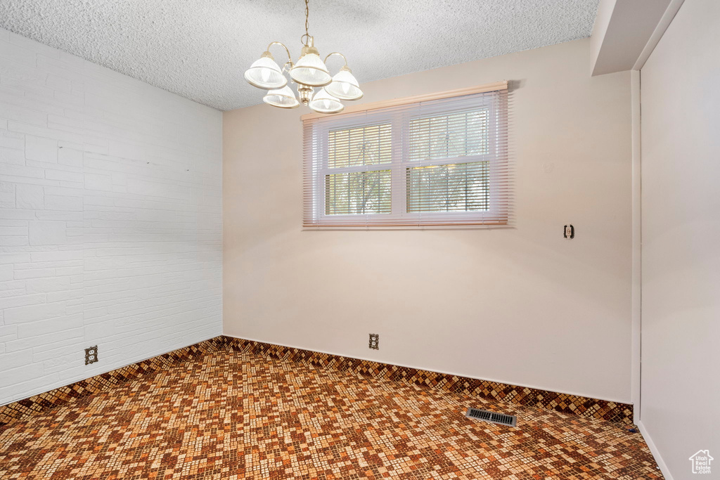 Empty room with an inviting chandelier and a textured ceiling