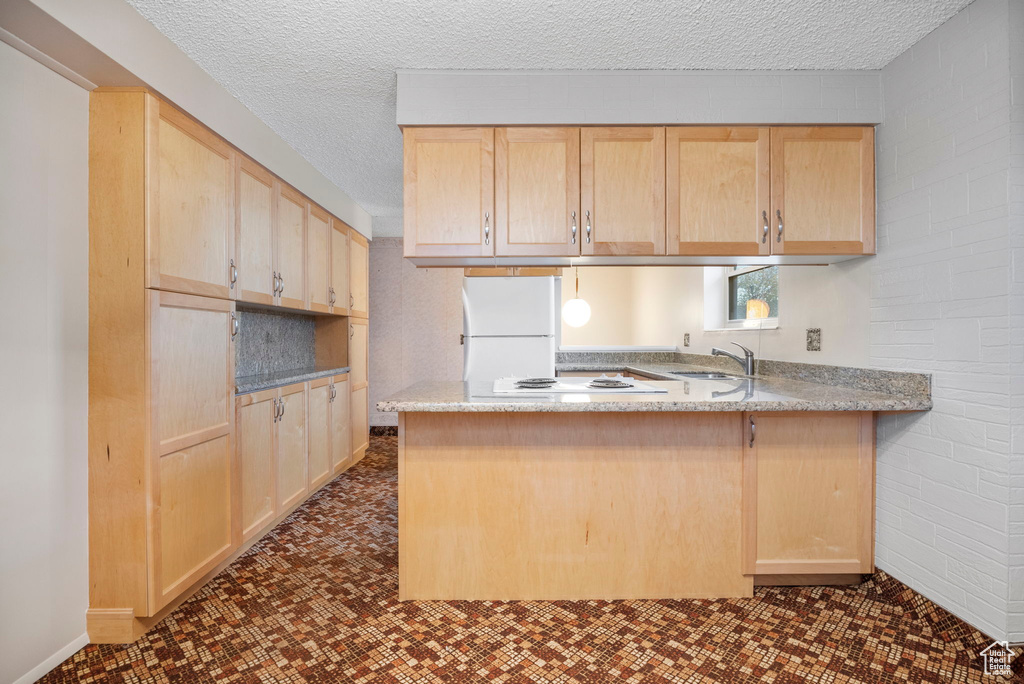 Kitchen with white appliances, a textured ceiling, light brown cabinetry, and kitchen peninsula