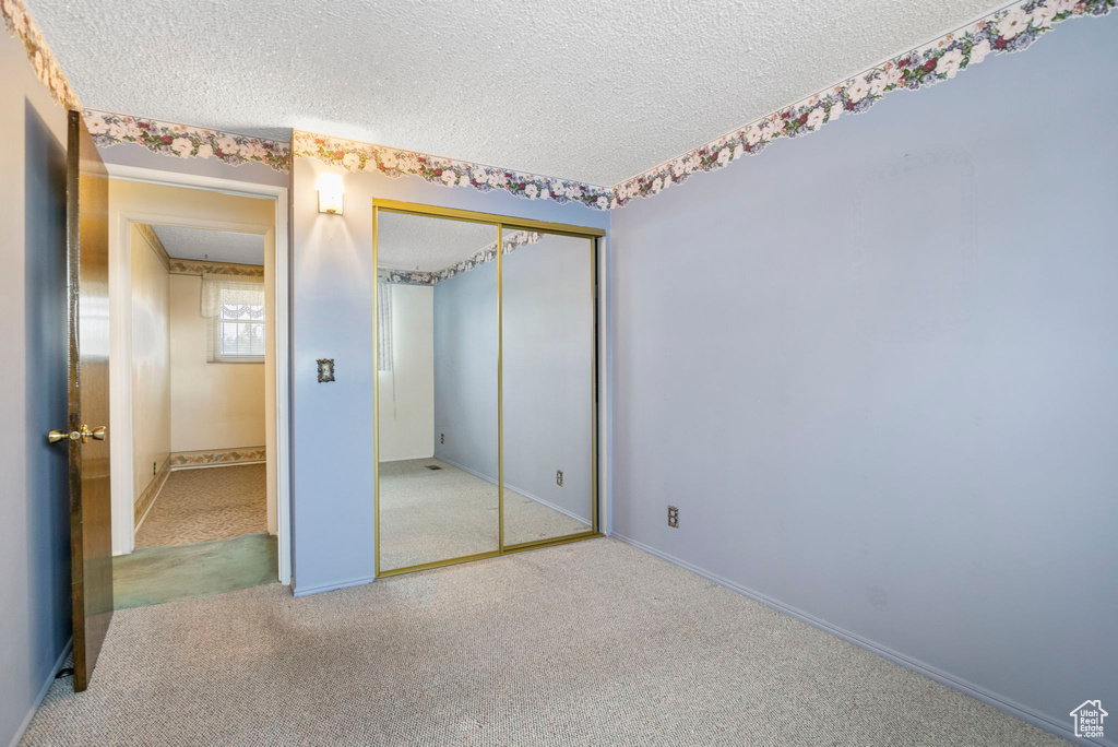 Unfurnished bedroom featuring a closet, a textured ceiling, and light colored carpet