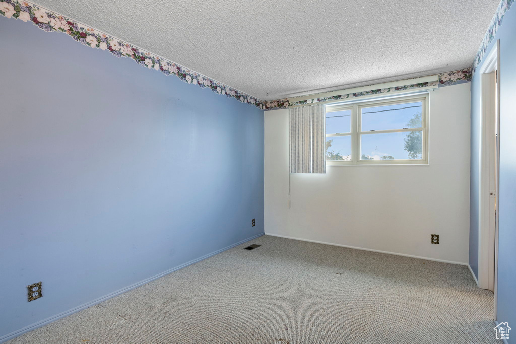 Empty room featuring a textured ceiling and carpet floors