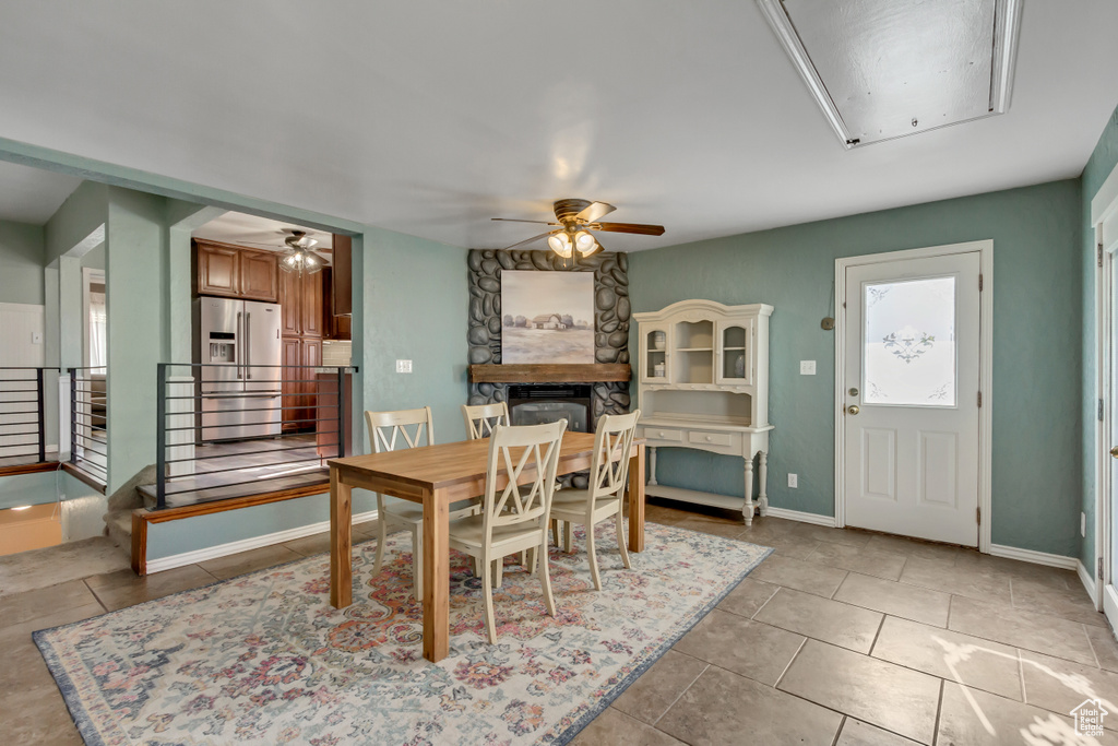 Dining area featuring a stone fireplace, light tile patterned floors, and ceiling fan