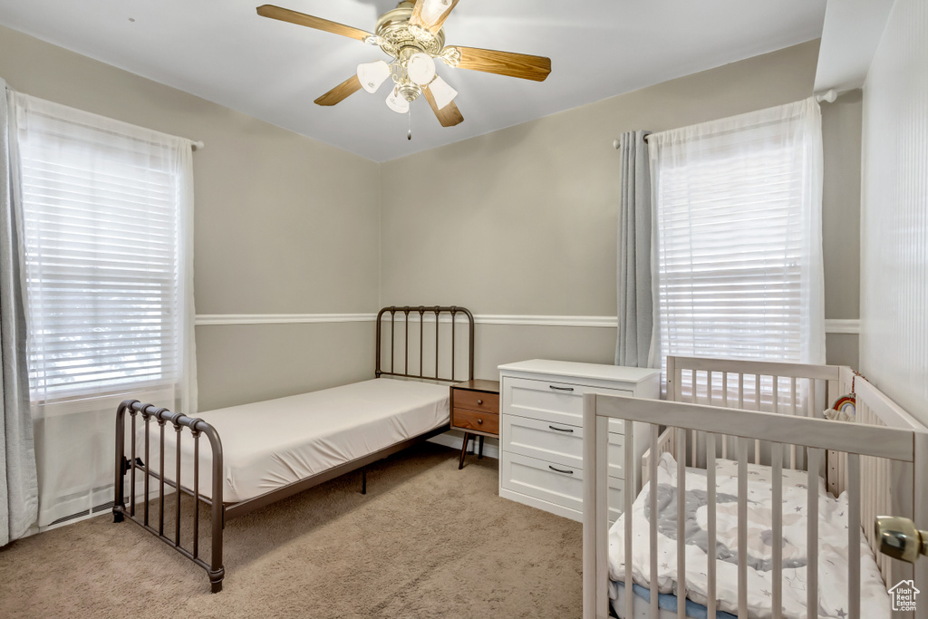 Carpeted bedroom featuring ceiling fan and a crib