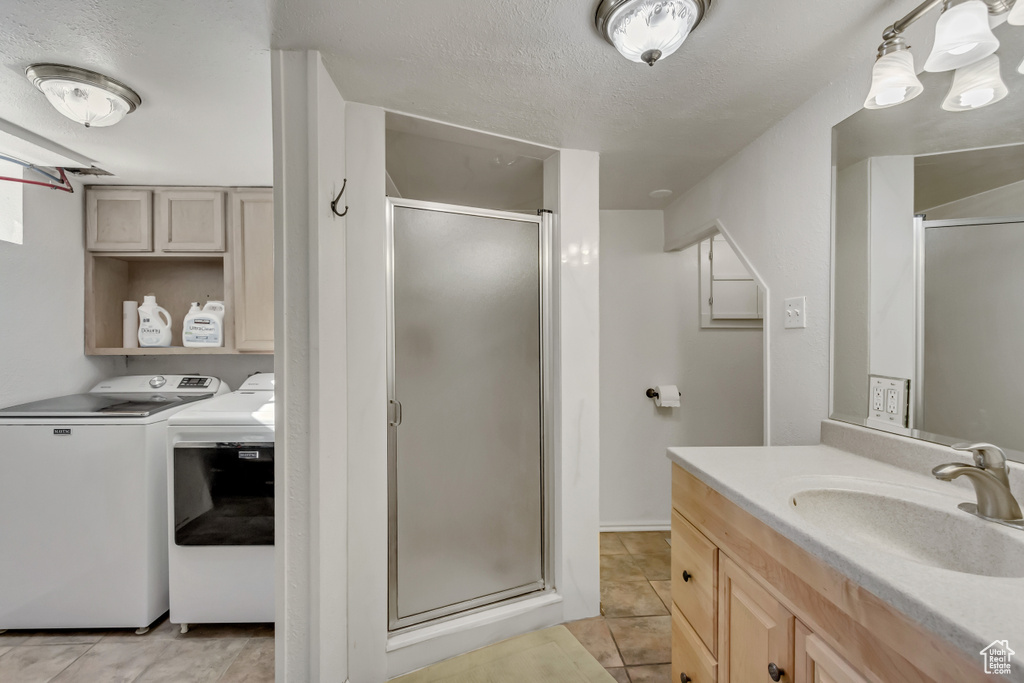 Bathroom with a textured ceiling, washer and clothes dryer, vanity, a shower with shower door, and tile patterned floors