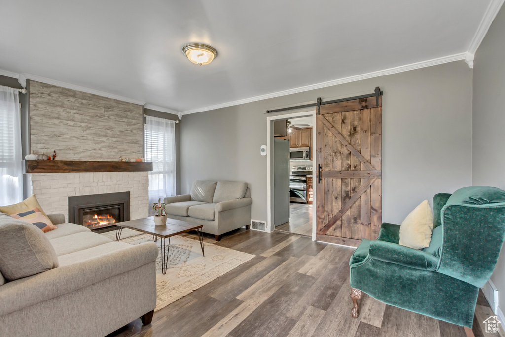 Living room featuring ornamental molding, hardwood / wood-style floors, a barn door, and a stone fireplace