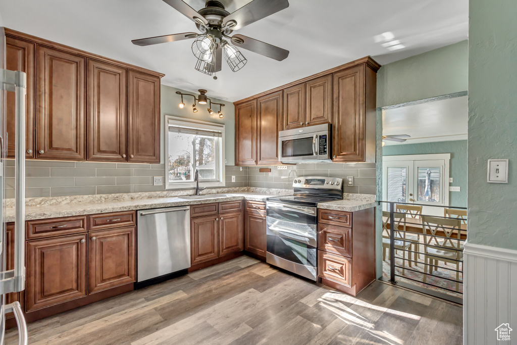 Kitchen featuring light stone counters, stainless steel appliances, decorative backsplash, sink, and light hardwood / wood-style floors