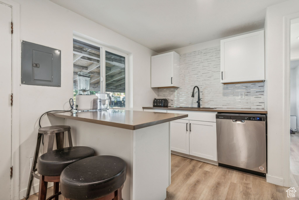 Kitchen featuring white cabinetry, sink, a breakfast bar, stainless steel dishwasher, and kitchen peninsula