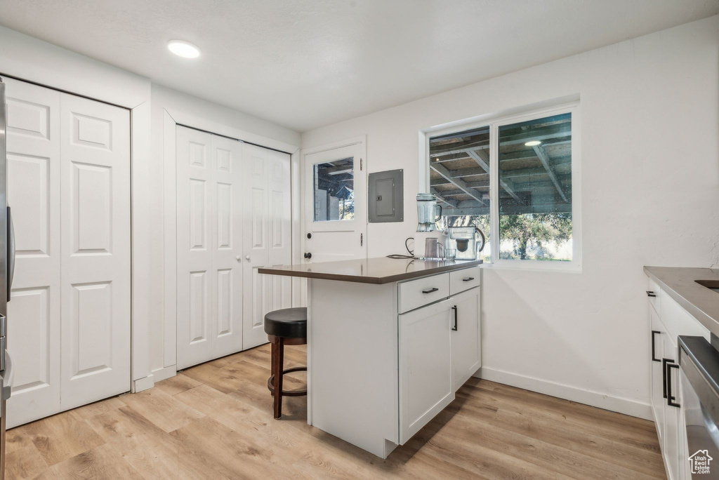 Kitchen with white cabinetry, a breakfast bar, kitchen peninsula, electric panel, and light wood-type flooring