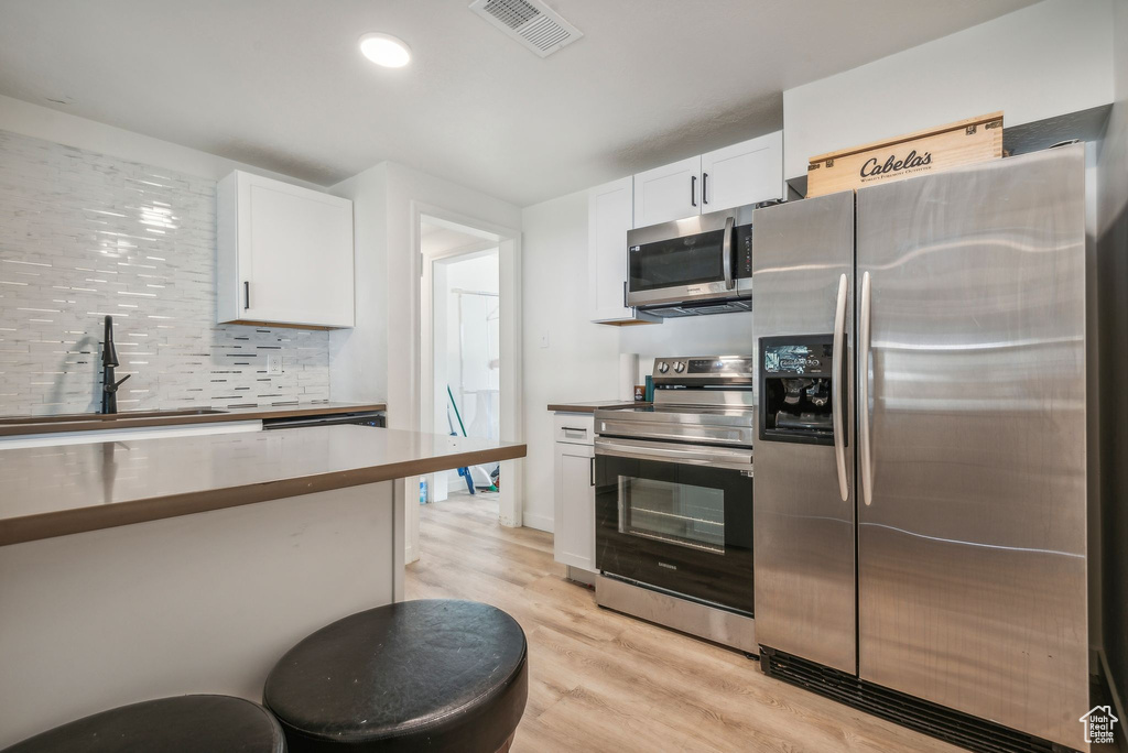 Kitchen with white cabinetry, appliances with stainless steel finishes, decorative backsplash, and light hardwood / wood-style floors