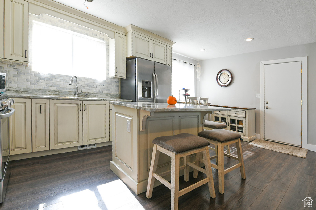 Kitchen featuring dark hardwood / wood-style floors, cream cabinets, appliances with stainless steel finishes, and a center island