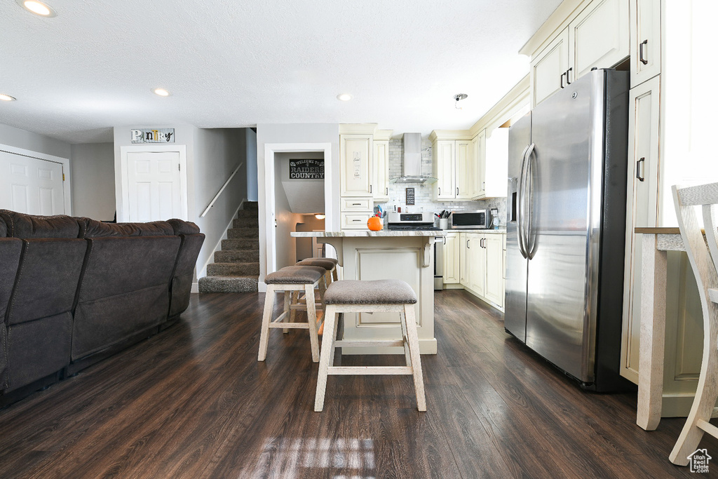 Kitchen featuring stainless steel appliances, wall chimney range hood, dark hardwood / wood-style flooring, a breakfast bar, and a center island