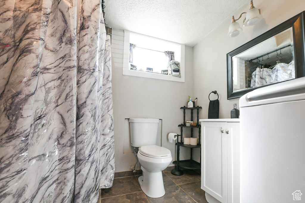 Bathroom featuring toilet, a shower with curtain, a textured ceiling, and tile patterned flooring